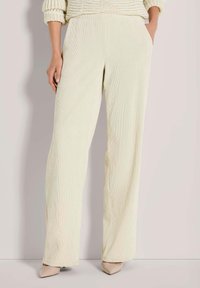 Vrouw die crèmekleurige wijde corduroy broek met zakken draagt, gecombineerd met beige puntige schoenen en een chunky gebreide trui.