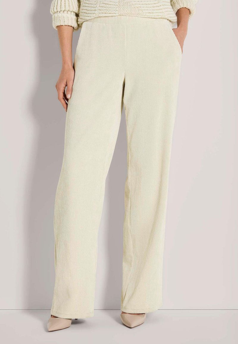 Vrouw die crèmekleurige wijde corduroy broek met zakken draagt, gecombineerd met beige puntige schoenen en een chunky gebreide trui.