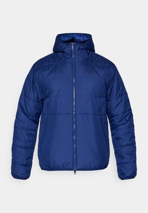 Zila izolēta jaka ar kapuci, kurai ir kvadrātveida raksts, priekšējais rāvējslēdzis un diskrēts logotips uz krūtīm. Gluda materiāla apdare un pielāgota piegriezuma forma.