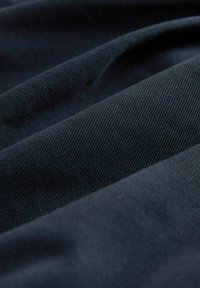 Tmavě námořnická tkanina s diagonálním ribkováním a jemným leskem, která obsahuje složené záhyby pro vrstvený vzhled.