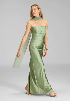 Satin, trägerloses, grünes Abendkleid mit geraffter Textur und einem fließenden Schal-Detail, ergänzt durch goldene Sandaletten mit Absatz.