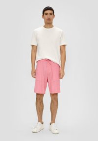 Roze korte broek van een gestructureerde stof, met een trekkoord in de taille en twee voorzakken, gecombineerd met een plain witte T-shirt met korte mouwen en witte sneakers.