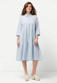 Vestido azul claro con cuello, mangas tres cuartos, frente con botones y falda en capas y fluida. Hecho de una tela ligera.