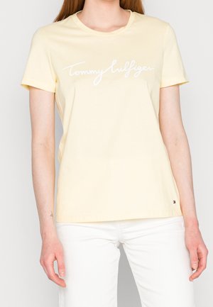 Light yellow cotton t-shirt featuring a white script logo "Tommy Hilfiger" across the chest. Short sleeves, round neck, and subtle hem detailing.