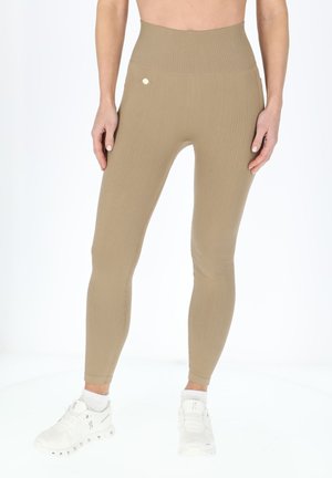Beige højtaljede leggings med ribbet tekstur og et lille guldlogo på taljen, parret med hvide sportsko.