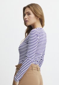 Langærmet bluse med vandrette lilla og hvide striber, ribbet tekstur og en tætsiddende silhuet, parret med højtaljede beige bukser.
