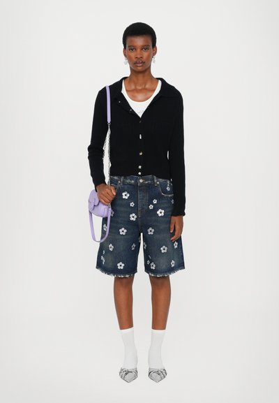 Black ribbed cardigan, white t-shirt, blue denim shorts with floral embroidery, paired with white socks and silver-patterned shoes, holding lilac bag.
