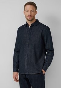 Camicia di denim scuro con chiusura a bottone, colletto a punta e maniche lunghe. Il materiale sembra resistente e ha una texture liscia. Nessun motivo o accenti.