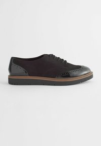 Crne suede modne cipele s sjajnim crnim lakiranim detaljima, brogue ukrasima i smeštim gumom. Okrogli vrh i vezivanje na vezice.