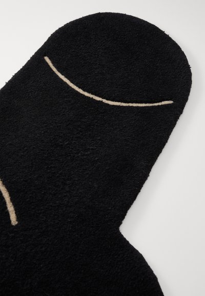 Zwarte vloerkleed met een pluche textuur, gevormd als een figuur, met een prominent beige gebogen lijndetail. Zacht, modern ontwerp.