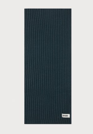 Écharpe tricotée vert foncé avec texture côtelée et une petite étiquette blanche portant la mention "DRYKORN" à une extrémité.