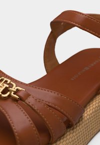 Καφέ πλατφόρμα δερμάτινο σανδάλι με χρυσή μεταλλική αλυσίδα και υφασμένο πάτο, διαθέτει λουράκι στον αστράγαλο και πολλαπλά λουράκια στο μπροστινό μέρος.