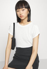 Camiseta branca de manga curta, feita de tecido suave, combinada com uma saia preta de altura elevada. Uma pequena bolsa preta pende da alça do ombro.