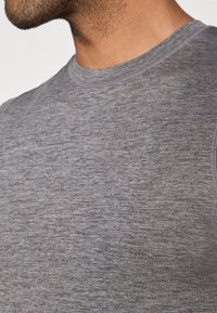 Γκρι αθλητικό τοπ με μαλακό, υφασμάτινο ύφασμα. Διαθέτει στρογγυλή λαιμόκοψη και διακριτική λεπτομέρεια με λογότυπο κοντά στο στήθος.