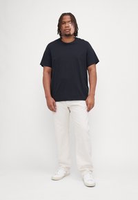 Camiseta negra de manga corta, corte relajado, combinada con pantalones beige claros. Zapatillas blancas completan el conjunto. Diseño sencillo de un solo color.