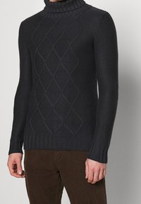 Maglione a collo alto lavorato a maglia scura con motivo a rombi, polsini e orlo a costine. Realizzato in tessuto spesso e testurizzato per garantire calore.