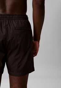 Zwarte zwembroek met een elastische tailleband, voorzien van een ritssluiting op de achterzak en een lichte, gladde textuur.