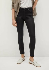 Jeans ajustados negros con cintura alta y una textura suave, combinados con mocasines blancos y un blazer de cuadros estructurado.