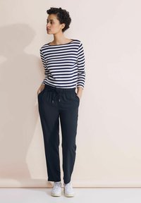 Marineblauw en witte gestreepte long-sleeve top gecombineerd met zwarte elastische taillebandbroek en witte sneakers. Gladde stof, losse pasvorm en casual ontwerp.