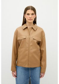 Karma brune kunstlæderjakke med lynlås foran, to forlommer og nitter på kraven. Glat tekstur, afslappet design og løs pasform.