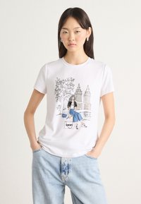 T-shirt en coton blanc avec un imprimé graphique d'une fille aux cheveux gris assise près de bâtiments. Coupe décontractée avec des manches courtes et un col rond.