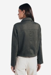 Olivkowa krótka kurtka wykonana z miękkiego materiału, z płaskim kołnierzem, długimi rękawami i detalami na plecach.