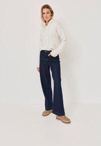 Felpa crema con coulisse, abbinata a jeans svasati blu scuro e scarpe con plateau marrone chiaro. Texture liscia e vestibilità casual.