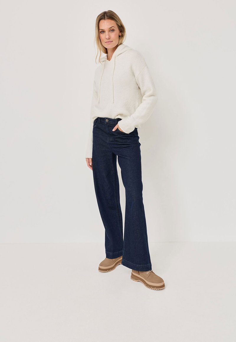 Felpa crema con coulisse, abbinata a jeans svasati blu scuro e scarpe con plateau marrone chiaro. Texture liscia e vestibilità casual.