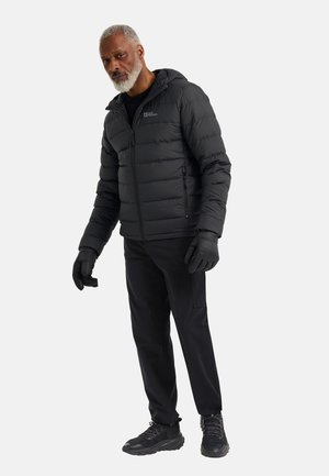Schwarze Steppjacke mit Kapuze, vorne mit Reißverschluss und Bündchen. Kombiniert mit schwarzen Handschuhen, Hose und robusten schwarzen Schuhen.