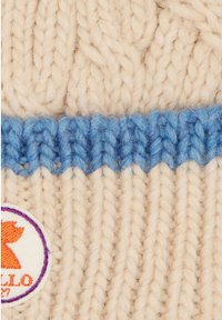 Knit beanie in cream with a blue band, featuring textured stitching and a round, embroidered logo in purple with a red accent.