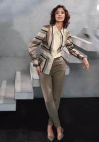 Beige patroonhemd met geometrische ontwerpen, gecombineerd met olijfgroene broeken. Gladde textuur, aangevuld met spitse beige schoenen.