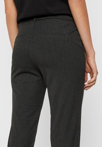 Pantaloni grigi scuri con tessuto strutturato, vita elastica e due tasche posteriori, mostrati dalla prospettiva posteriore.