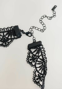Black lace choker with intricate floral patterns. Features a textured clasp and a chain extension for adjustable length.