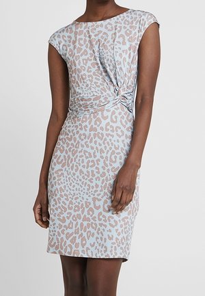 Femme portant une robe courte à manches courtes, longueur genou, imprimé léopard bleu clair et beige avec un détail de nœud torsadé à la taille.