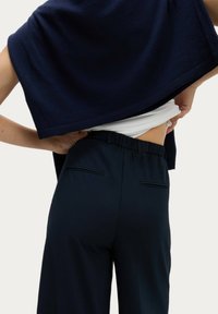 Marinblå stickad tröja hängande över en vit topp, kombinerad med marinblå byxor med elastisk midja och två bakfickor. Slät textur.