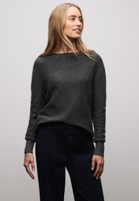 Pull léger gris avec un col large et des poignets côtelés, associé à un pantalon bleu marine, présentant une texture lisse et une coupe décontractée.