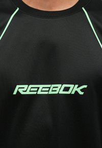 Čierne športové tričko s krátkym rukávom, s mätovo-zeleným logom Reebok a tenkými mätovo-zelenými akcentmi pozdĺž ramien.