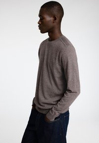 Brun langermet strikkegenser med rund hals, med en avslappet passform og ribbestrikkede mansjetter, parret med mørkeblå denimjeans.