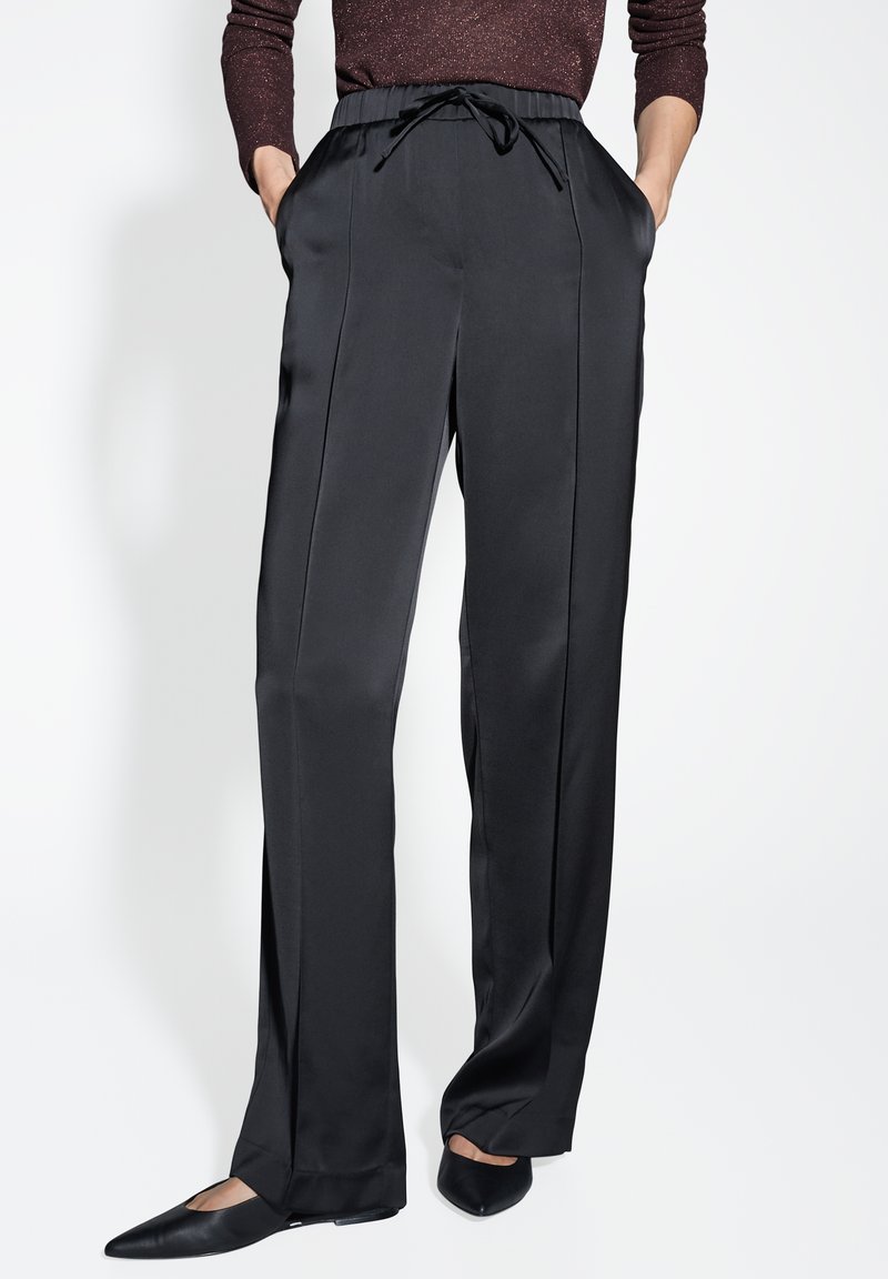 Pantaloni neri a gamba larga realizzati in un tessuto liscio e leggero. Presentano un elastico in vita con coulisse e tasche laterali. Parte anteriore piatta con linee eleganti.