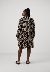 Robe à manches longues présentant un motif abstrait noir et beige. Fabriquée dans un tissu léger avec une coupe décontractée et un col rond.