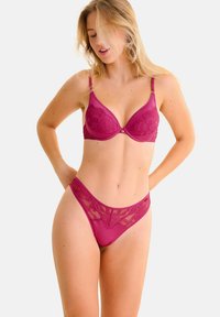 BH en string set in diep magenta, met een vrouwelijke kanten overlay en een gladde stof. De BH heeft gevoerde cups en verstelbare bandjes.
