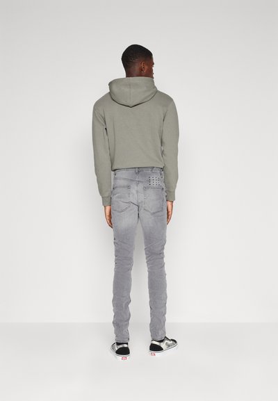 Felpa grigia con coulisse, abbinata a jeans grigi chiari con borchie decorative sulla tasca posteriore. Sneakers bianche e nere.
