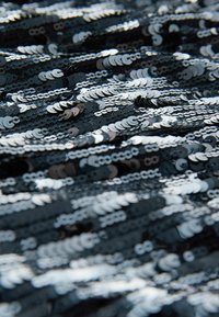 Gros plan d'un tissu noir densément recouvert de sequins argentés brillants créant une surface texturée et réfléchissante.