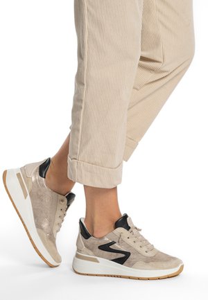 Beige sneakers with a metallic finish, black leather accents, and textured fabric. Features a white sole and lace-up design.