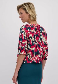 Kleurige, gebloemde blouse in rood, blauw en crème; heeft korte, gerimpelde mouwen en een relaxte pasvorm. Textuurstof met een abstract motief.