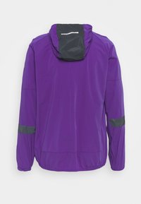 Giacca impermeabile viola con cappuccio nero, riflessi sulle maniche e polsini elasticizzati per una vestibilità sicura. Tessuto morbido e leggero.