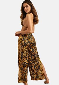 Tenue à imprimé floral avec un fond noir et des motifs botaniques dorés. Le haut présente des bretelles croisées, et le pantalon large a des fentes sur les côtés.