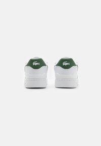 White sneakers with a green accent on the heel, featuring a textured logo and smooth leather upper, with a sturdy rubber sole.