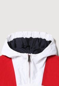 Rode en witte jas met hoge kraag, voorzien van een ritssluiting en elastische capuchon. Het interieur is gevoerd met marineblauw.