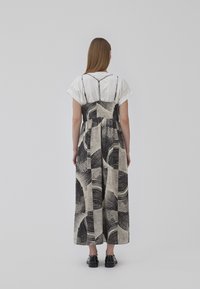 Robe longue noire et blanche à motif, fabriquée en tissu texturé, avec des bretelles larges et une coupe ample, associée à des chaussures noires.